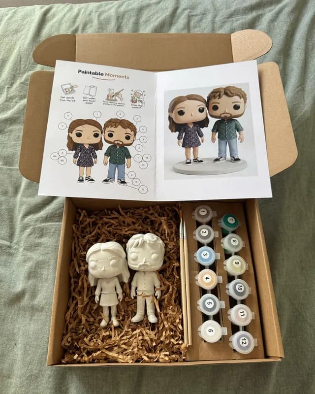 Freshly opened PaintableMoments kit with two unpainted figurines, paints and the painting guide