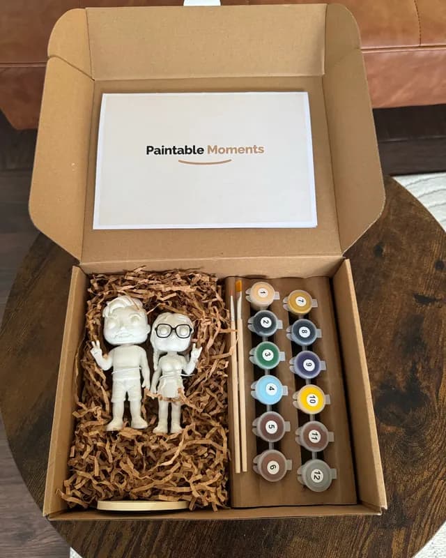Opened kit with two figurines, one wearing glasses, next to numbered paint pots